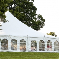 a white wedding tent set up in a lawn surrounded by trees and with the sides down